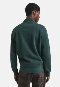 Donkergroene pullover trui met een hoge kraag, geribbelde manchetten en een reguliere pasvorm. De stof lijkt zacht en heeft een lichte textuur.