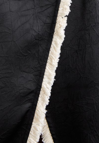 Material negru cu o textură șifonată, având o margine ciufulită de culoare crem pe o parte. Designul este simplu și în contrast accentuat.
