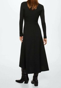 Černé dlouhé šaty s přiléhavým korzetem, rozšířenou sukní a texturovanou látkou. Doplněno nadkolenními černými botami s robustním podpatkem.