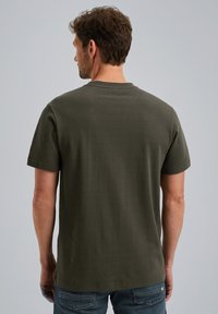 Camiseta de manga corta de color verde oliva, hecha de tejido texturizado. Presenta un escote redondeado y un corte regular, usada con jeans azules.