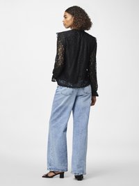 Svart blonderbluse med lange ermer, bølgete kanter og blomster mønster; kombinert med løse blå jeans og svarte hælsandaler.