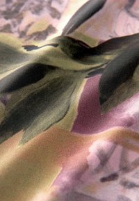 Tekstil med en glat, mat overflade og en farveblanding af grønne, pink og sorte abstrakte mønstre, der skaber et blødt, lagdelt udseende.