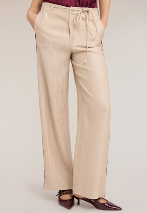 Beige weit geschnittene Hosen mit gebundener Taille und Taschen, kombiniert mit bordeauxfarbenen Pumps mit Absatz und spitzer Zehenpartie.