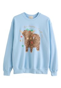 Jasnoniebieska bluza bawełniana z grafiką brązowego, puszystego zwierzaka, ozdobioną ostrokrzewiem, ozdobami i napisem. Prosty dekolt typu crew neck.