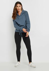 Maglione in cotone blu con colletto ampio e orlo con coulisse, abbinato a leggings neri e sneaker bianche. Tessuto morbido, vestibilità rilassata.