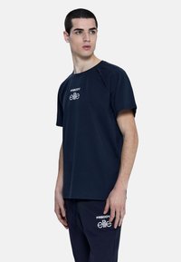 T-shirt in cotone blu navy con maniche corte, scollo rotondo e dettagli del logo bianco sul petto. Texture liscia, vestibilità comoda.