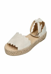 Beige suede espadrille sandal with scalloped design, woven jute outsole, ankle strap, and open toe. Flat heel for added comfort.