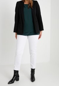 Blazer nero su un top teal, abbinato a pantaloni bianchi e stivali anklet in pelle lucida nera. L'outfit presenta linee sartoriali e una vestibilità classica.