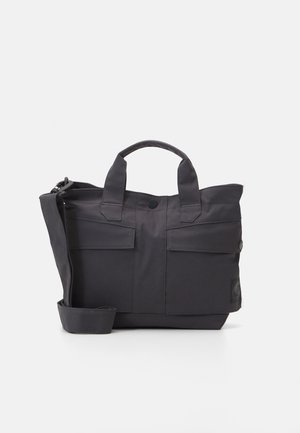 Bolso tote negro hecho de tela duradera, con dos bolsillos frontales, asas cortas y una correa de hombro desmontable. Cierre ajustable.