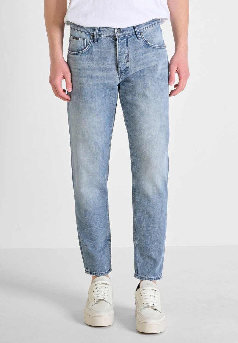 Jeans de mezclilla azul claro con un diseño de pierna recta, desvanecimiento sutil, estilo de cinco bolsillos y costuras en contraste. Combinados con zapatillas blancas.