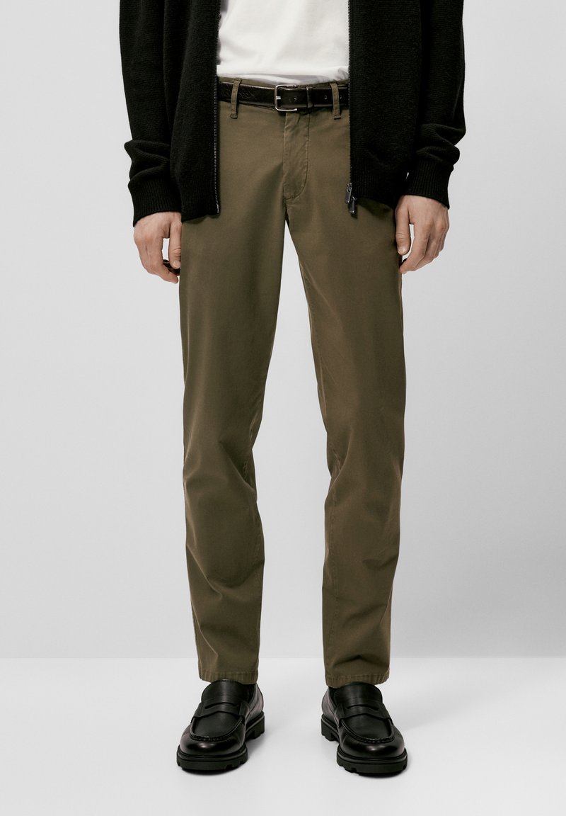 Khaki broek, van katoen, rechte pasvorm, ceintuurlussen, ritssluiting, gecombineerd met zwarte instappers en een zwarte cardigan. Smooth textuur.