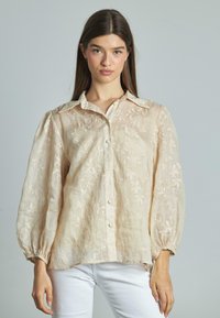 Blusa ricamata di un beige chiaro, con chiusura a bottoni, colletto e maniche voluminose con polsini elasticizzati; realizzata in un tessuto trasparente e testurizzato.
