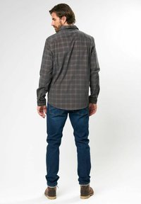 Camisa de cuadros gris con cuello puntiagudo, mangas largas, dobladillo curvado, y jeans azul oscuro, combinada con botas marrones.