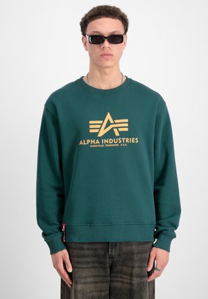 Grøn sweatshirt lavet af blødt materiale, med et guld logo "ALPHA INDUSTRIES" og stribet design. Ribbet halsudskæring og mansjetter.