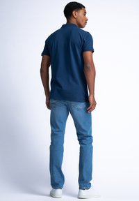 Námořnická polo košile s límečkem, krátkým rukávem a rovním lemem, v kombinaci se světlomodrými džíny a bílými teniskami.