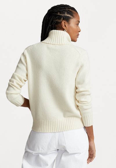 Cream-colored knit sweater with a high collar, ribbed cuffs, and waistband. Features a textured pattern and fitted silhouette.