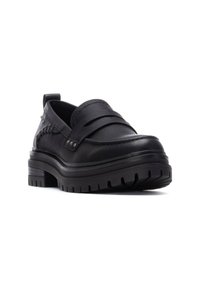 Mocasines de cuero negro con múltiples ranuras, superficie texturizada y una gruesa suela de goma con un patrón de dibujo. Los acentos incluyen costuras decorativas.
