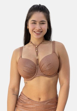 Lächelnde Frau mit langen dunklen Haaren trägt ein schimmerndes bronzenes Bikinioberteil und passenden Bikiniunterteil, ergänzt durch eine Halskette und kleine Ohrringe.