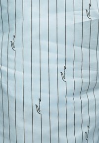 Tissu bleu clair avec de fines rayures verticales noires et de petits motifs d’alligator brodés en noir, espacés de manière régulière.