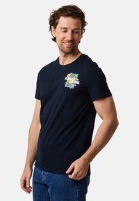 Navy blå bomulds T-shirt med rund halsudskæring, der har et livligt trykt design med blomster og tekst på venstre brystområde.