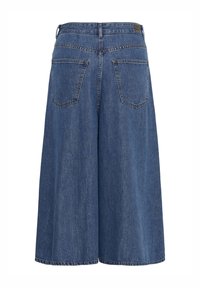 Short en denim bleu à jambes larges, taille haute, poches arrière, passants pour ceinture, avec une petite étiquette en cuir sur la ceinture.