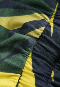 Textil med gröna, gula och marinblå ränder samt en skrynklig textur. Tyget har en samlad designdetail längs kanterna.