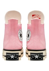 Baskets montantes en toile rose avec un logo blanc, une semelle noire et une plateforme de couleur crème. Elles présentent un arrière arrondi et des coutures visibles.