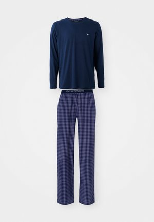 Tricou albastru închis cu mânecă lungă, având un logo mic, asociat cu pantaloni de pijama în carouri, cu un elastic la talie și culori contrastante.