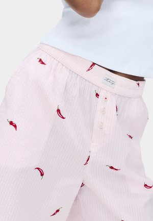 Pantaloni di cotone rosa chiaro con piccoli disegni di peperoncini rossi, chiusura con bottoni e top corto bianco a coste.