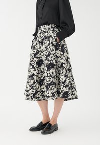 Svartvitt blommigt kjol med en utsvängd design, knä-lång, med fickor och en texturerad tyg. Buren med svarta loafers.