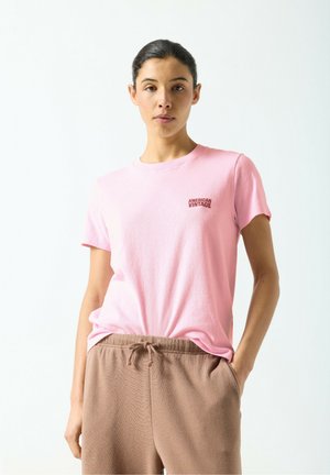 T-shirt en coton rose à manches courtes avec un col rond, arborant un petit logo "American Vintage" en rouge foncé sur le côté gauche de la poitrine.