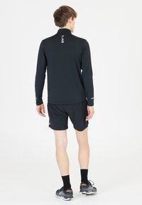Sort langærmet atletisk top med høj krave og reflekterende detaljer, parret med sorte shorts. Stoffet fremstår glat og let.