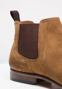 Stivale Chelsea in suede marrone con pannello elastico scuro ai lati, linguetta sul tallone e suola in legno stratificato.