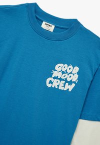 Niebieska bawełniana koszulka z okrągłym dekoltem, z białym nadrukiem "GOOD MOOD CREW" z przodu. Krótkie rękawy, miękka faktura.