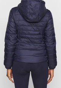 Marineblaue Steppjacke mit Kapuze, ausgestattet mit einem gesteppten Design, elastischen Bündchen und einer taillierten Silhouette. Glatte Textur und metallischer Reißverschluss.