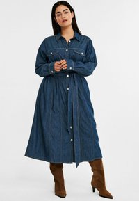 Denim-mekko, jossa on kauluskenttä, pitkät hihat, napitus ja sidottu vyötärö tummansinisenä, jossa on kontrastivärisiä ompeleita.