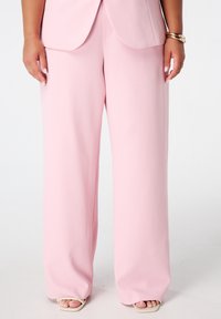Lichtroze wijde broek van gladde stof; gecombineerd met beige open schoenen. Het ontwerp heeft een relaxte pasvorm en strakke lijnen.