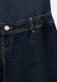 Ciemnoniebieskie dżinsy z srebrnym guzikiem, pomarańczowym przeszyciem, elastycznym pasem oraz częściowym widokiem granatowego topu powyżej.