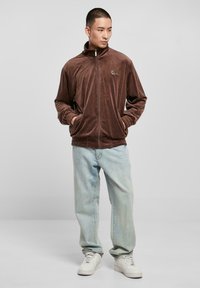 Brun fløyelsjakke med glidelås og høy krage, ribbestrikkede mansjetter og kant. Sammen med lyseblå, avslappede jeans og hvite sneakers.