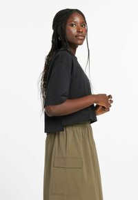 Camiseta negra recortada con mangas cortas, combinada con una falda caqui que tiene un bolsillo lateral y cinturilla elástica. Tejido de algodón suave.