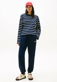 Maglietta a maniche lunghe a righe navy con righe bianche, abbinata a pantaloni jogger navy e sandali beige con suola nera spessa e dettagli in oro.