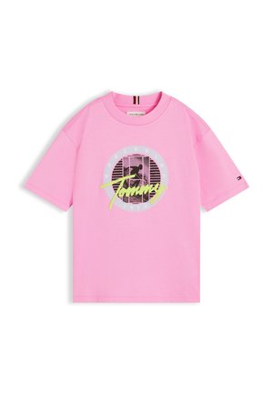 Ροζ κοντομάνικη μπλούζα με ασπρόμαυρο κυκλικό γραφικό, νεον κίτρινο κείμενο "Tommy" και μικρό λογότυπο σημαίας στο μανίκι.