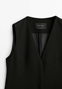 Gilet noir sans manches sur mesure avec un profond col en V et une étiquette de marque visible à l'intérieur du col.