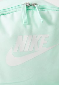 Mochila Nike em tecido menta suave, com um logótipo branco proeminente e puxadores de zíper prateados em uma superfície texturizada.