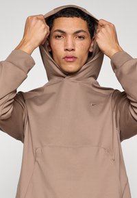 Καφέ φούτερ με κουκούλα και λεία υφή, με μπροστινή τσέπη και μικρό κεντημένο λογότυπο στο στήθος.