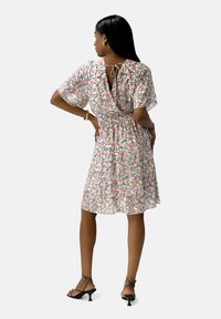 Kleid mit Blumenmuster, kurzen, flatternden Ärmeln, tailliertem Gürtel und einer Bindung im Rücken. Die Farben umfassen Pink, Grün und Gelb.