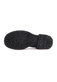 Semelle de botte en caoutchouc noir avec des crampons profonds et des motifs de grip en forme de croix sur fond blanc.
