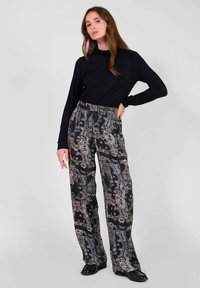 Haut à manches longues noir associé à un pantalon large à motifs avec un design paisley dans des tons de noir, blanc et crème. Texture de tissu lisse.