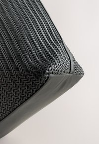 Sac tissé noir avec une surface texturée, fabriqué en matériau synthétique. Dispose d'un fond en cuir lisse et d'un design angulaire.