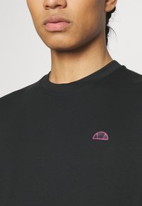 Black cotton t-shirt featuring a round neckline and a small pink embroidered logo on the chest. Smooth texture with short sleeves.
